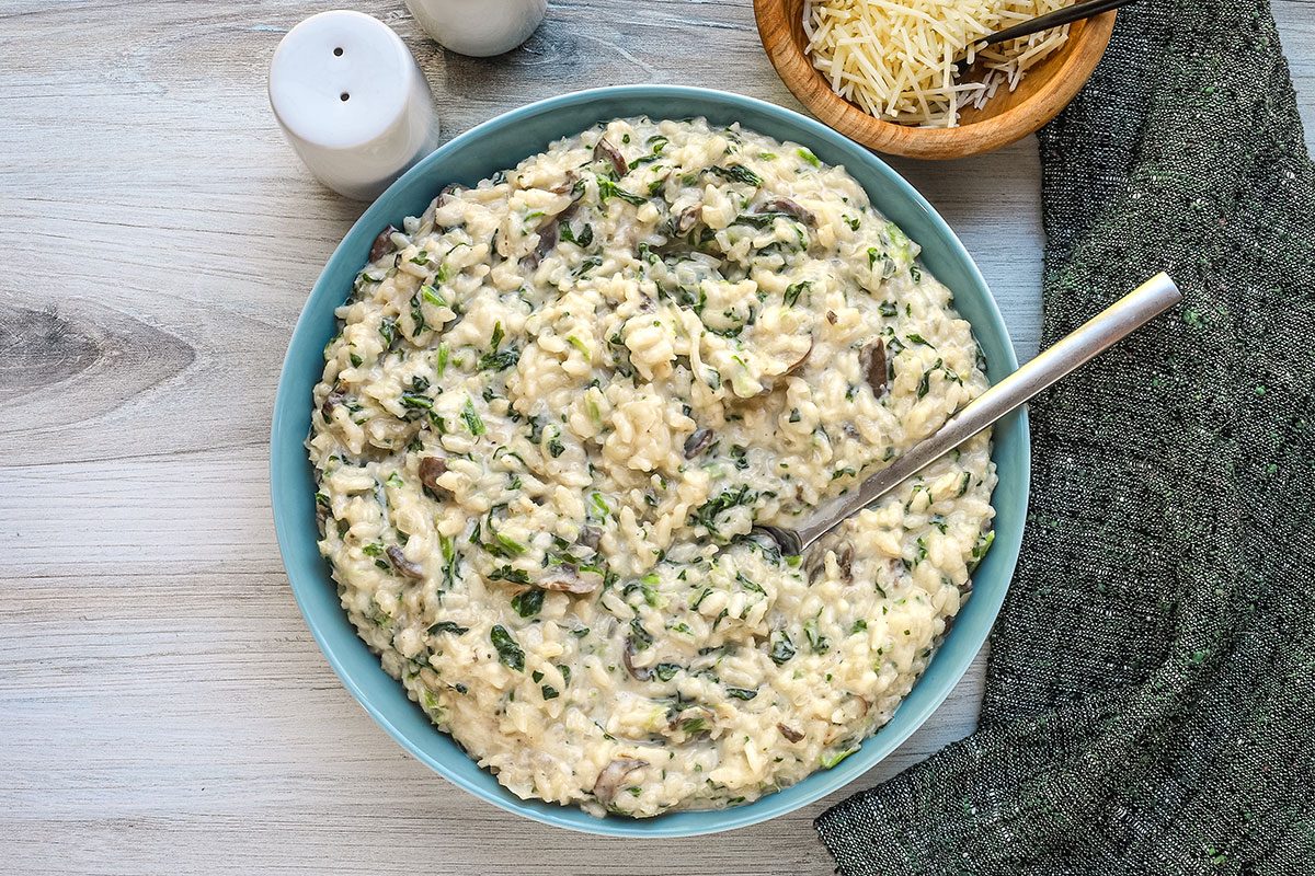 Hommade spinach risotto in a serving bowl with creamy Parmesan sauce and mushrooms.