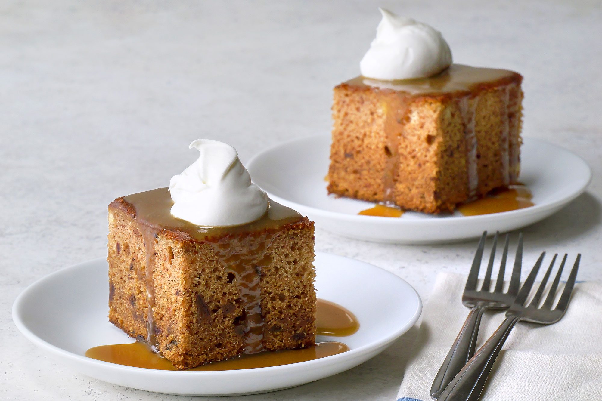 Table view shot of Sticky Toffee Pudding with Butterscotch Sauce; serve on two small plates; with fork and napkins; marble surface;