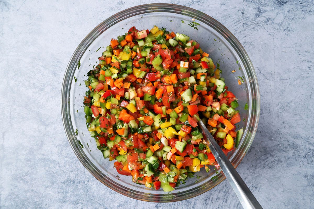 Process of making. Taste of Home's Israeli Salad in a large mixing bowl on a blue surface.