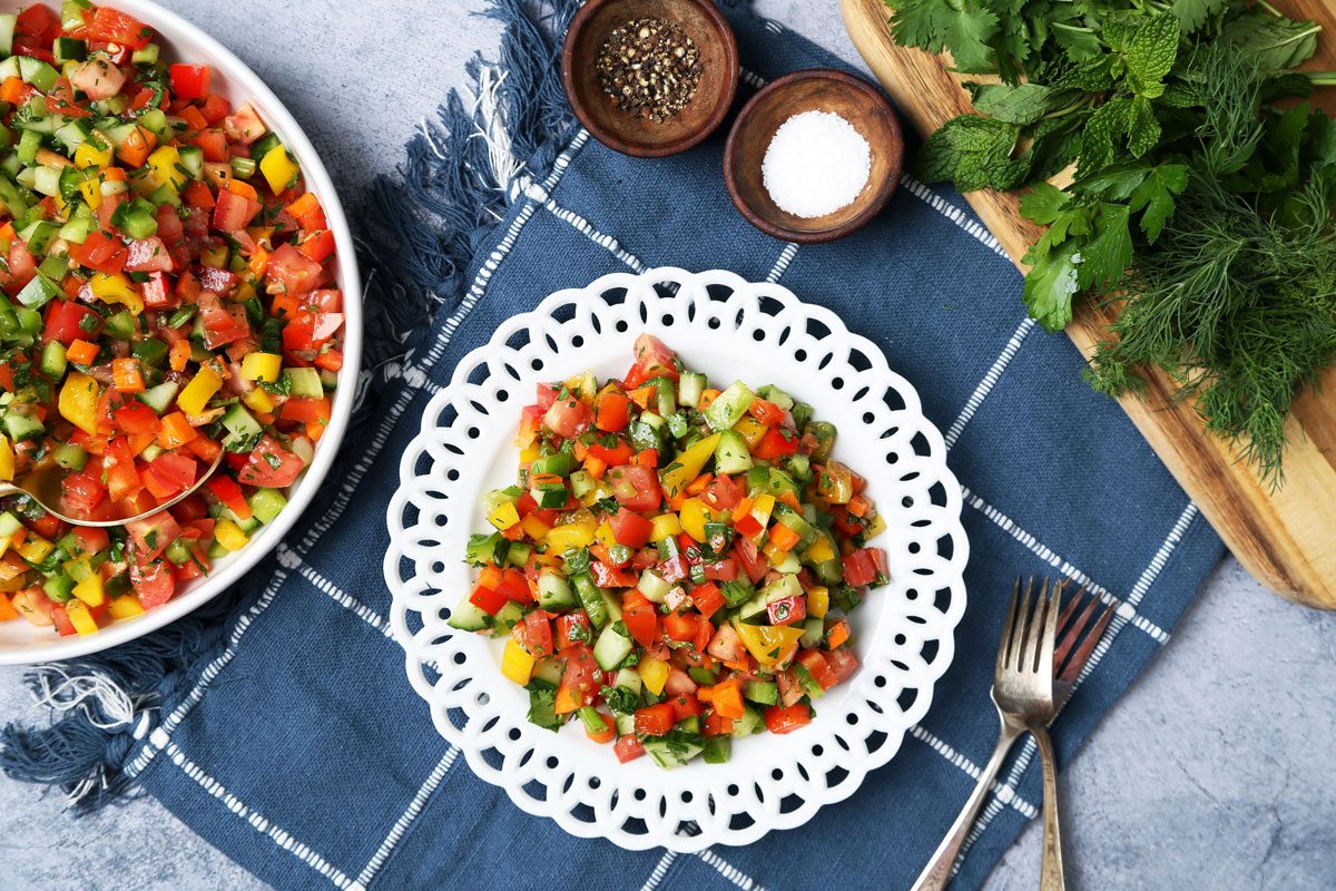 Close up of Taste of Home's Israeli Salad served on white plates on a blue linen and blue surface.