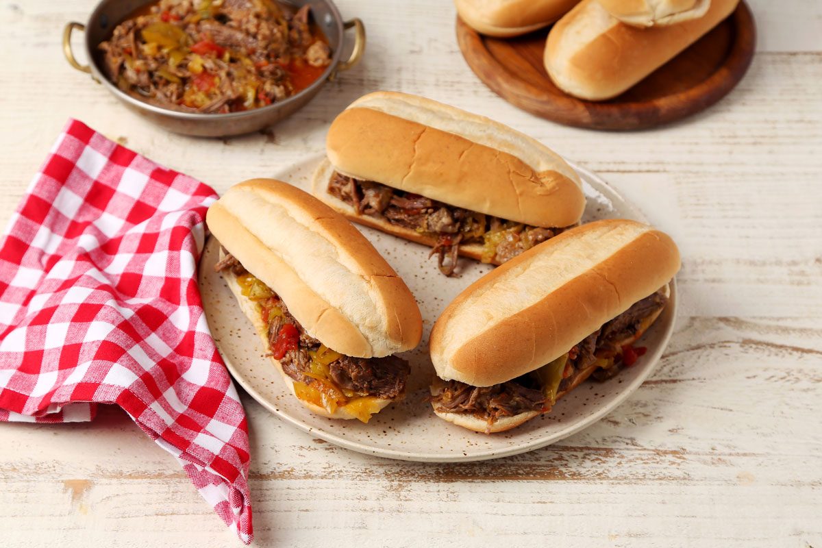 Close up of Taste of Home's Italian Beef Sandwiches served on a platter on a white wooden surface.