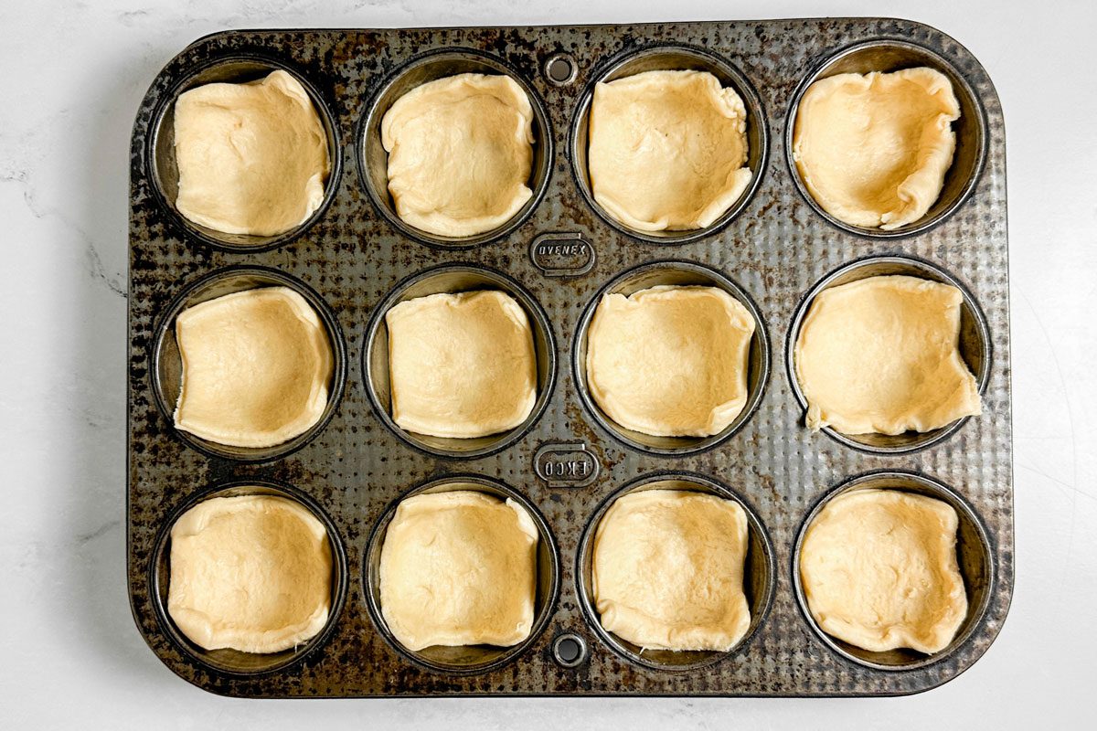 Crescent roll squares for Taste of Home Taco Cups in a vintage muffin tin on a marble surface