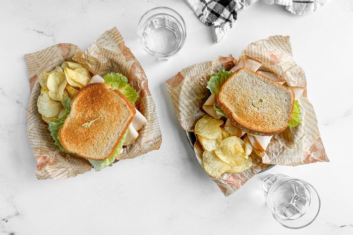 Taste of Home Turkey Avocado Sandwich on parchment lined metal plates with potato chips