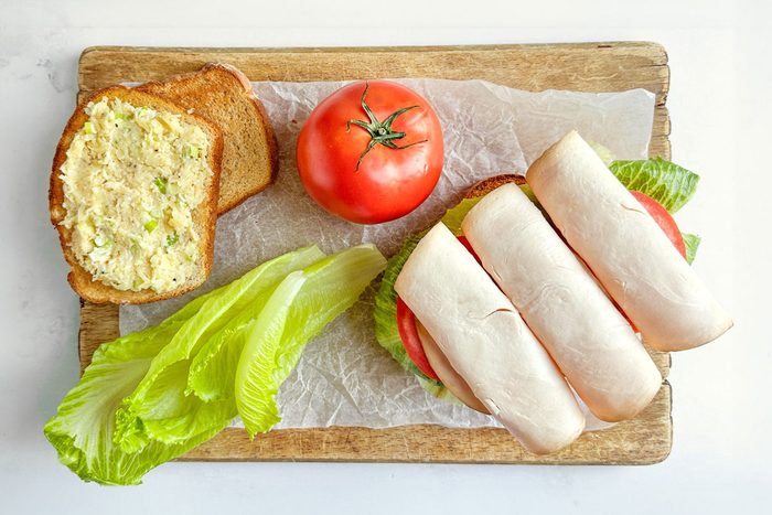 Taste of Home Turkey Avocado Sandwiches on a parchment lined wooden board with tomato and lettuce