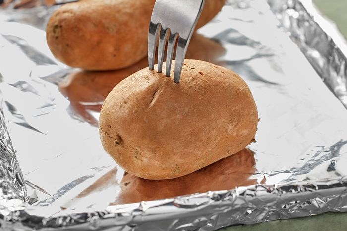 Baked potato on a foil sheet being poked with a fork.