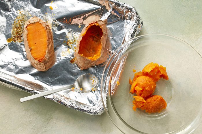 Baked potatoes on a foil sheet with a slice cut off from the top.