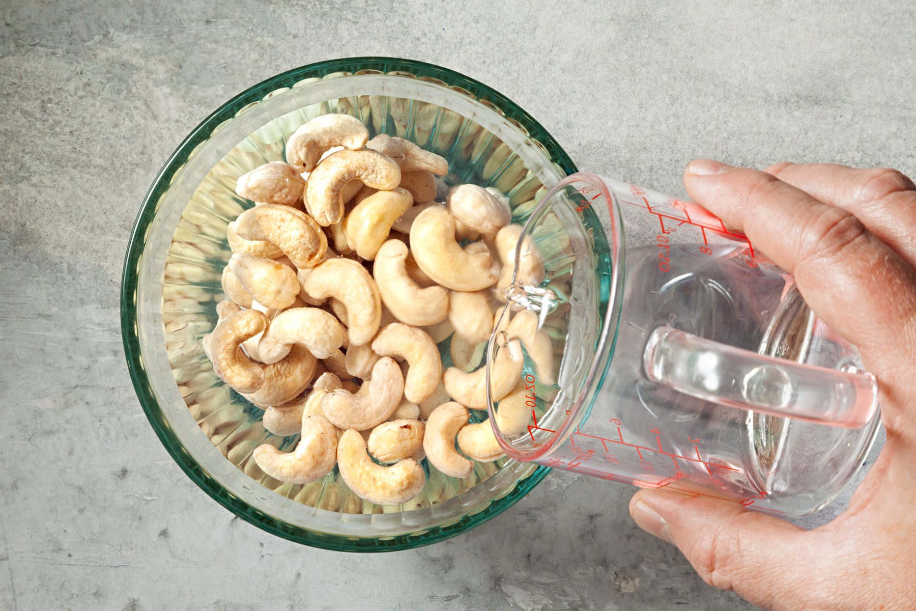 Overhead shot of place cashews a small bowl; and cover with water; soak overnight; grey marbel surface