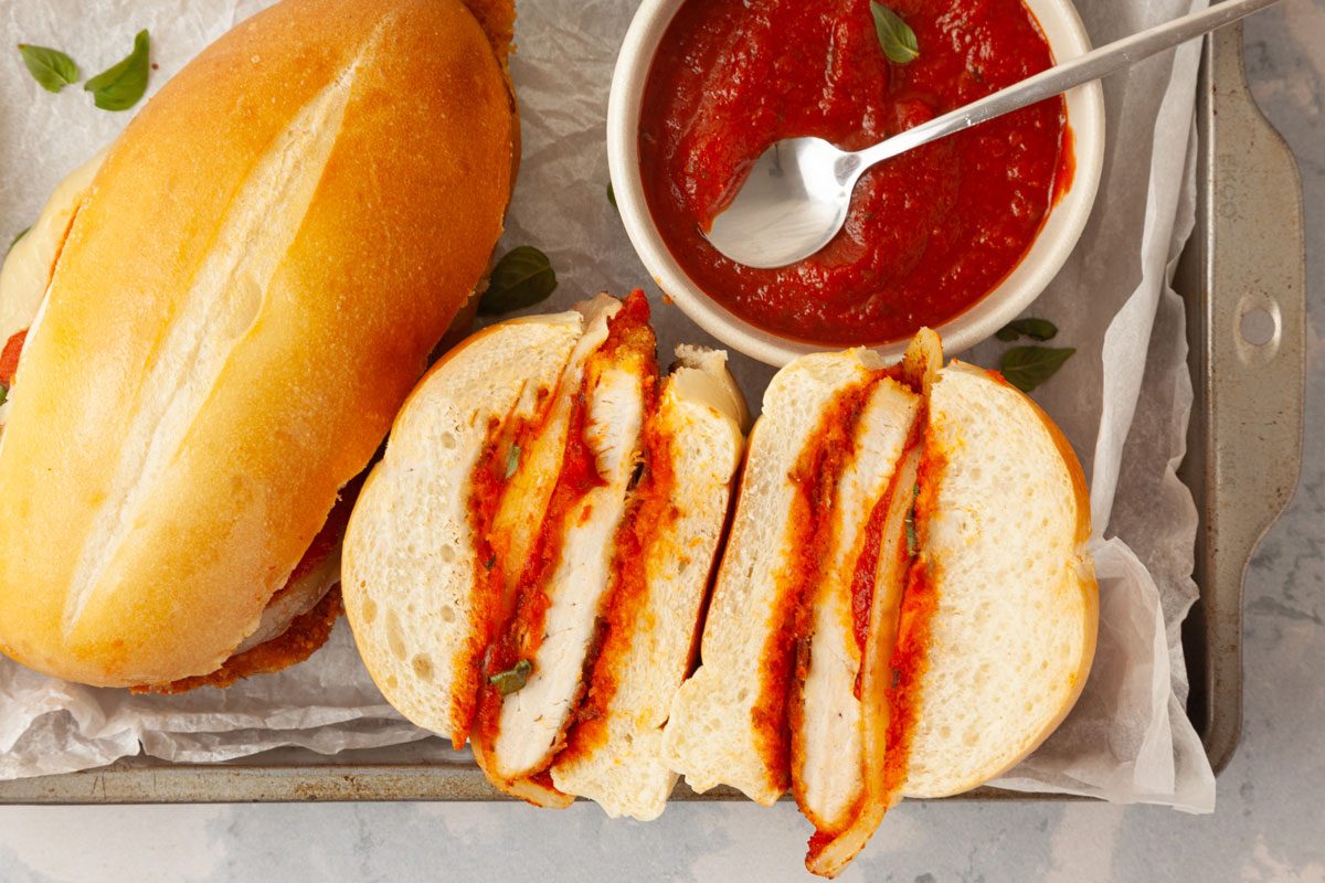 Two Taste of Home Parmesan Chicken Sandwiches with a bowl of marinara sauce on a metal tray