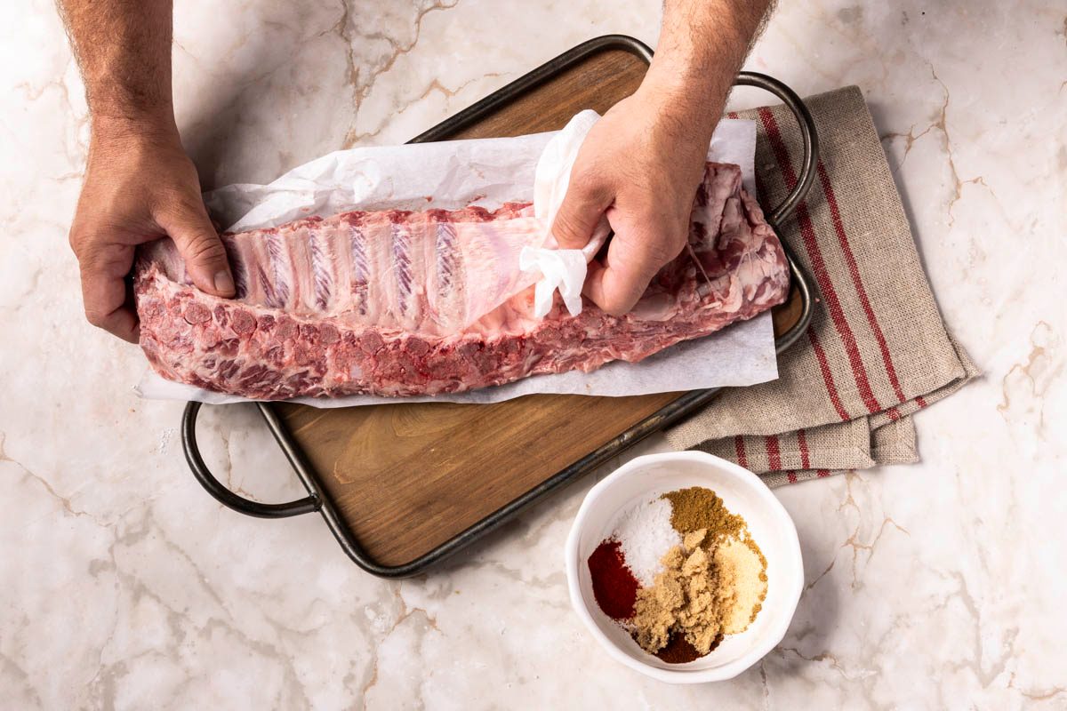 hand preparing Air-Fryer Pork Ribs next to seasoning on marble table shot at over head
