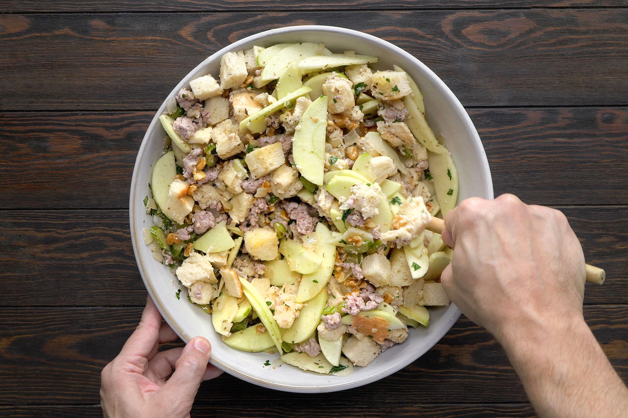 Adding cooked sausage to the celery mixture with bread cubes, apples, chicken broth and walnuts