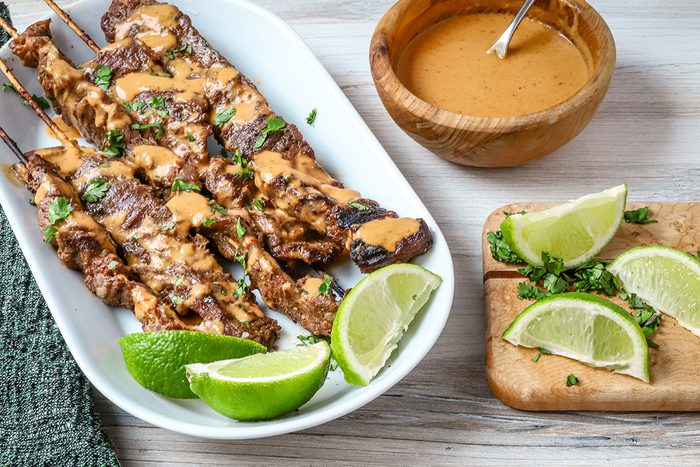 Beef satay with peanut sauce, lime wedges, and cilantro.