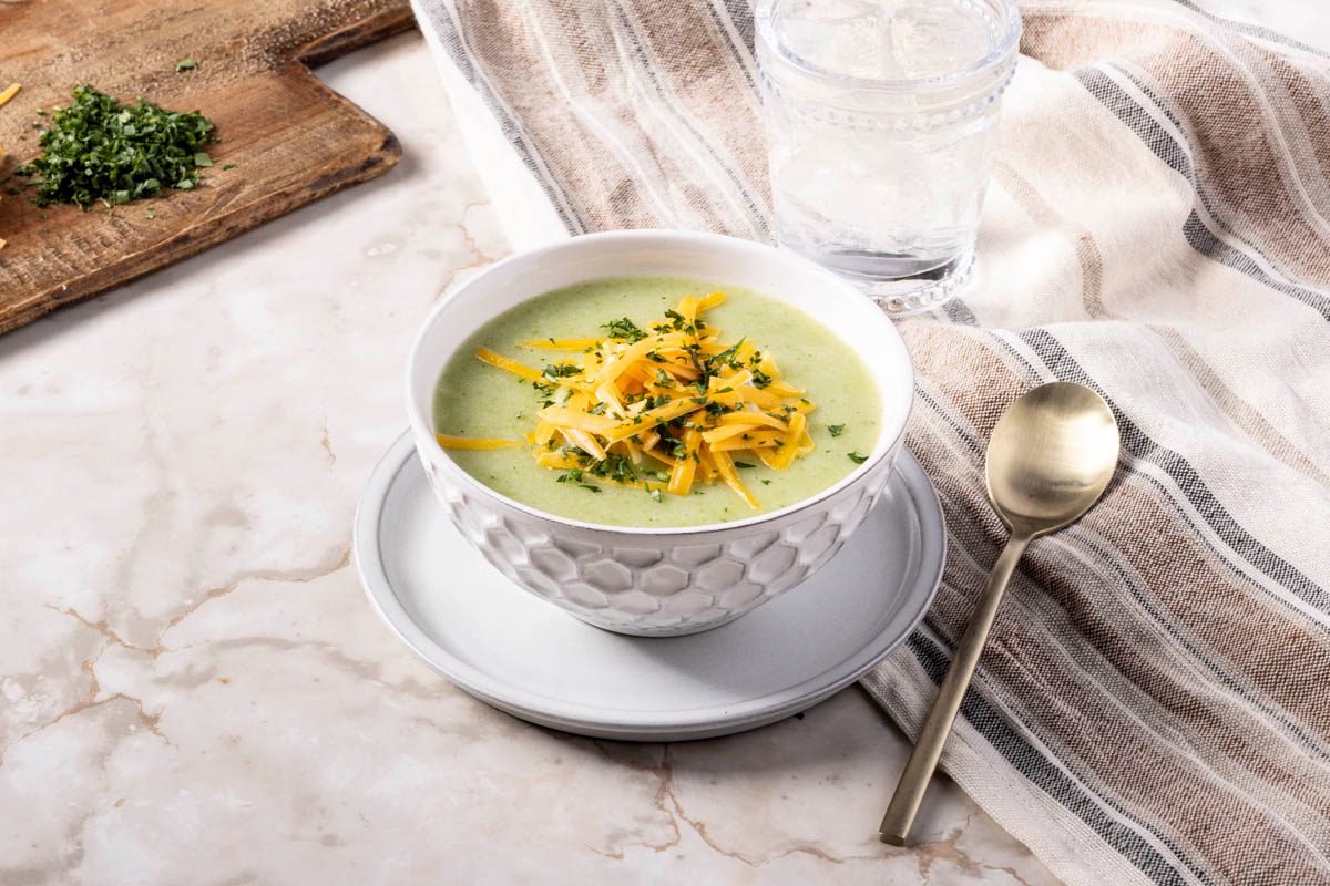 Broccoli Cheddar Potato Soup in a white bowl with a spoon on marble surface