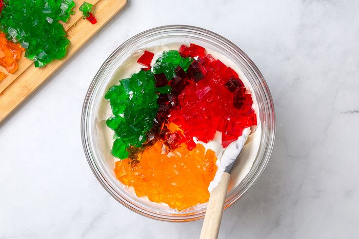 Cubed lime, strawberry and orange jello in a mixing bowl with cool whip and pineapple juice for step three for Broken Glass Jello recipe for Taste of Home