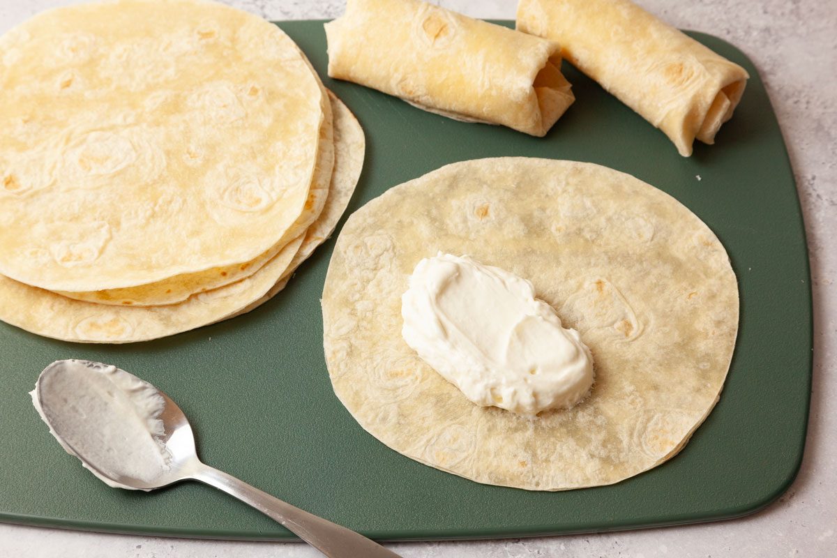 Step 2 of Taste of Home Cheesecake Chimichangas is to Lay each tortilla flat on a cutting board or baking sheet. Spoon two tablespoons of the cream cheese mixture into the center of each tortilla. Fold the sides of the tortilla in, over the filling, then roll tightly to form a chimichanga.