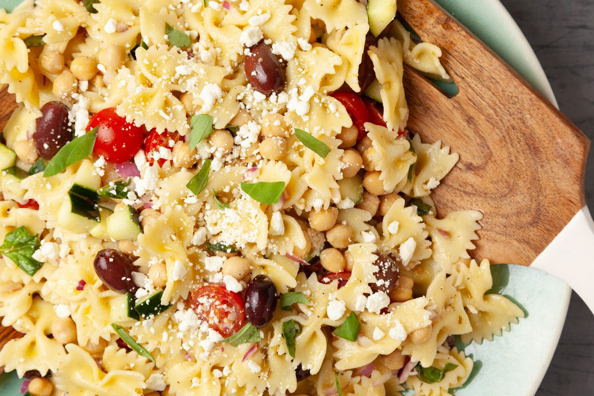 Close up of Full yield of Taste of Home Chickpea Pasta Salad in a light blue serving bowl, wooden salad servers