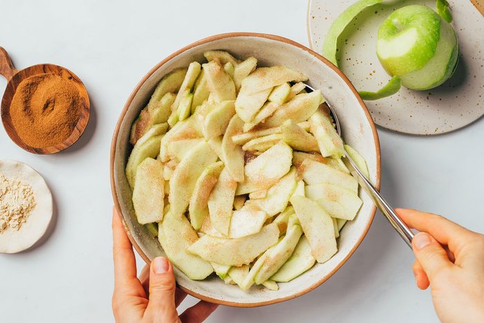 Mixing apple slices with sugar and cinnamon into a large bowl to make the fruit filling for the Cinnamon Apple Pie Recipe by Taste of Home