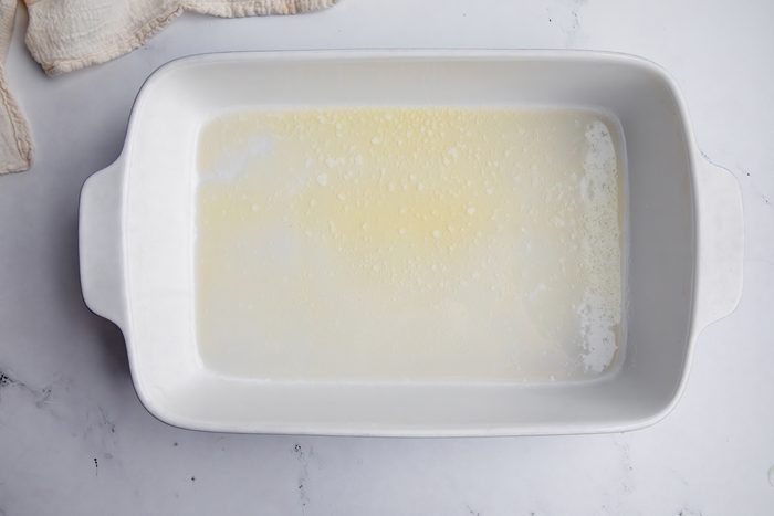 Overhead shot for Taste of Home Cornflake Chicken, melted butter in a large baking dish.