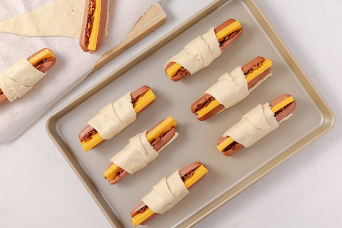 Hot dogs filled with cheese and bacon and wrapped with crescent rolls, ready to be baked.