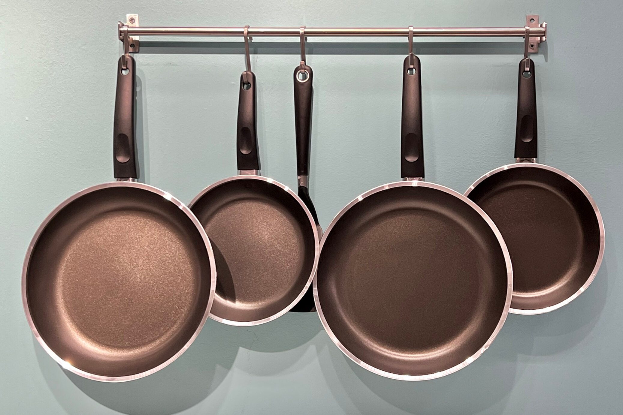 Set of kitchen metallic pans hanging on a pot rack in the kitchen