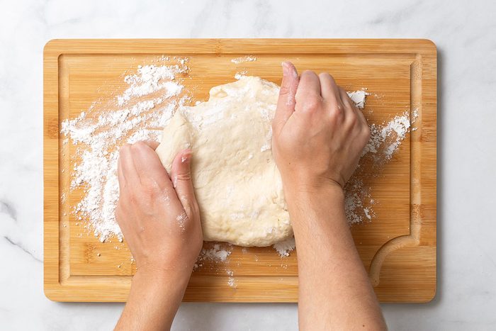 Kneading bread dough on floured wooden cutting board for step three of Homemade Breadsticks for Taste of Home