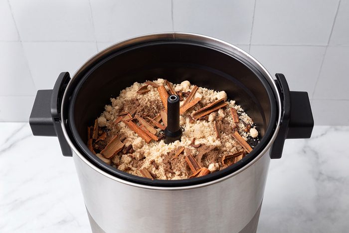 Filter basket of a large automatic percolator with brown sugar, cloves, allspice and cinnamon sticks for step one of Hot Apple Cider for Taste of Home