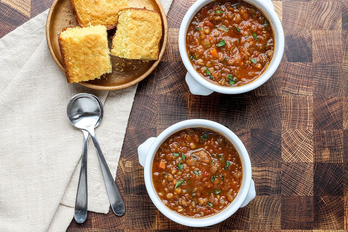 Overhead shot of Instant Pot lentil soup garnished with parsley and cornbread on the side.