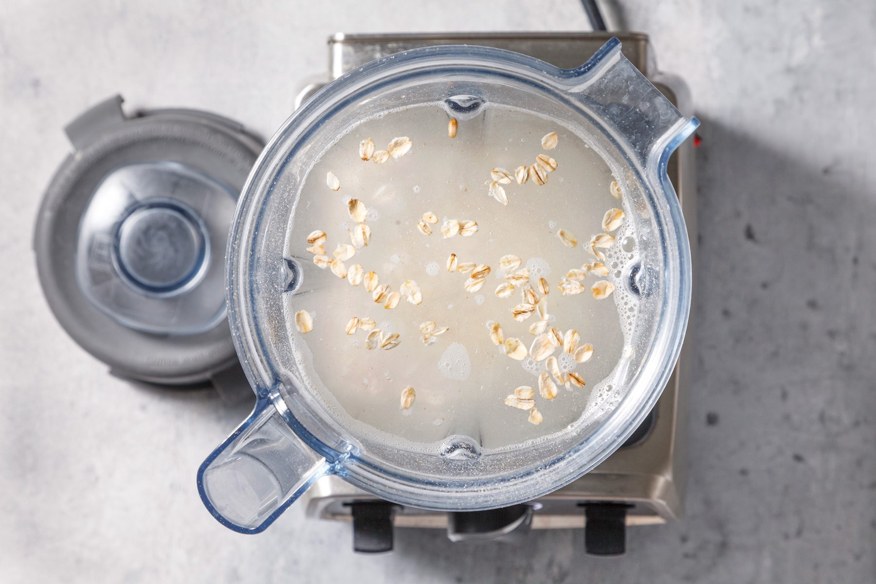 A jar on a blender containing a mixture of oats, water, maple syrup, and salt, ready for blending.