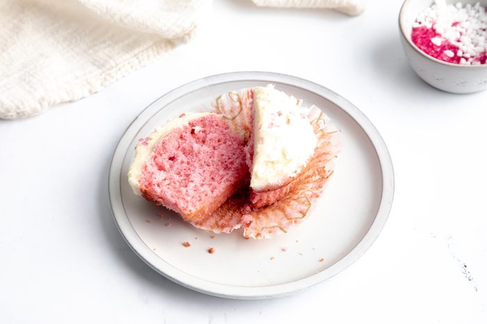 Close up beauty shot for Taste of Home Pink Cupcakes, cupcakes frosted and topped with sprinkles, cut open.