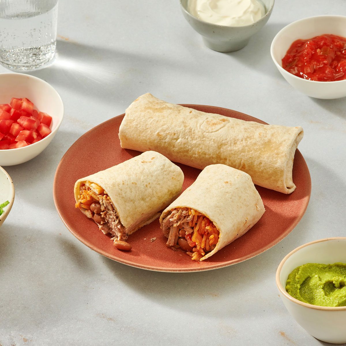 Pork burritos on a serving plate with garnishes on the side