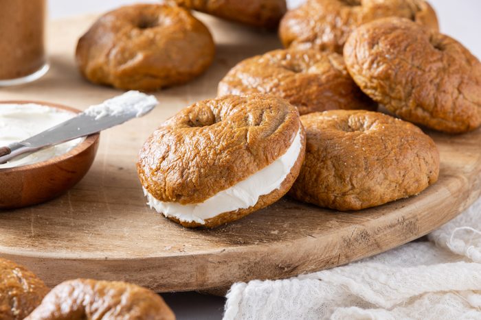 Bagels ready served on wood board, with detail of one bagel filled with cream cheese.