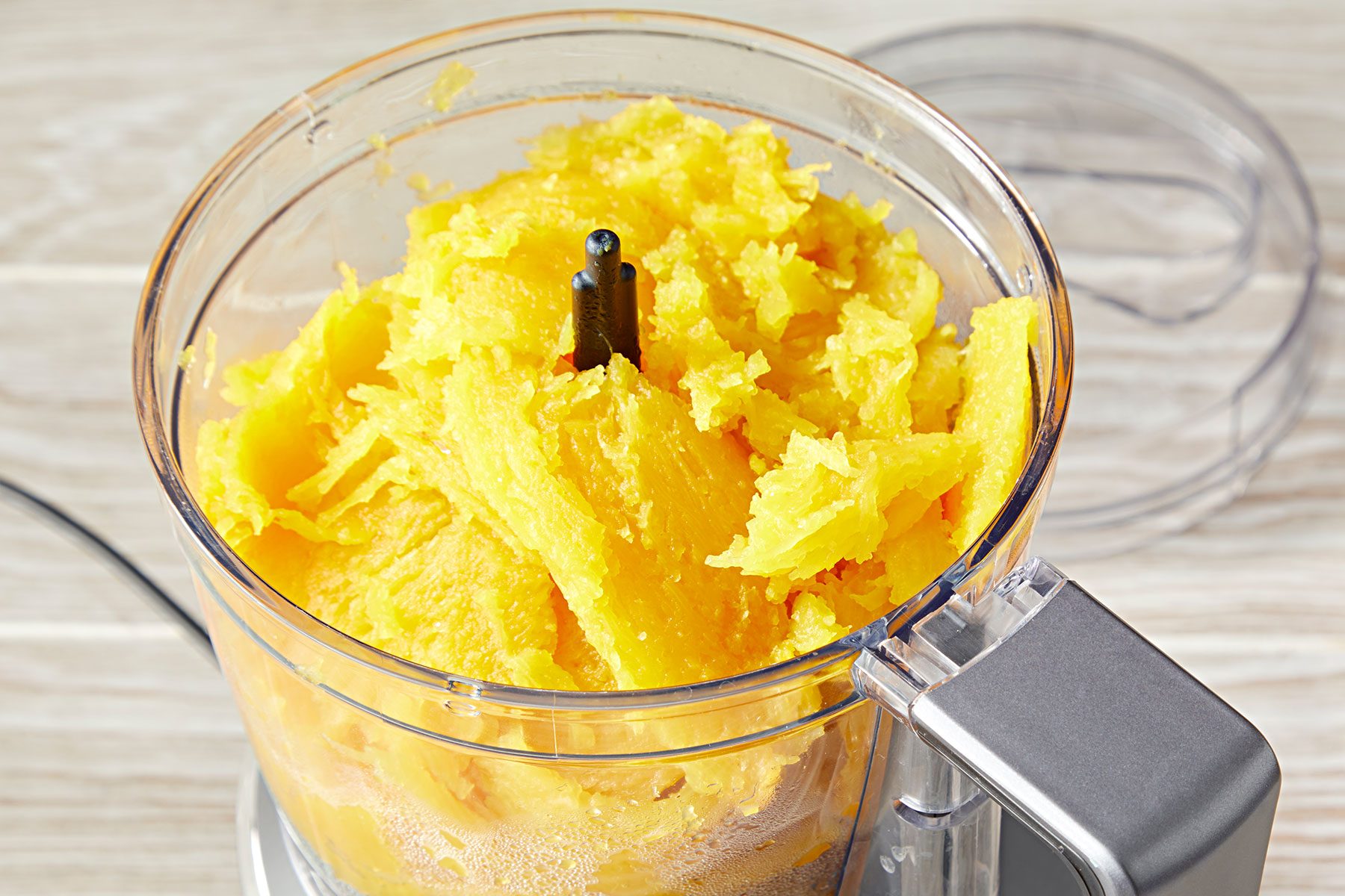 A food processor containing shredded pumpkin on a wooden surface.