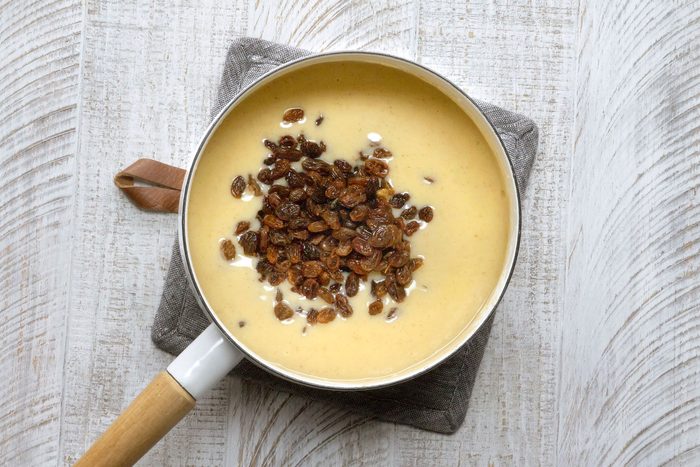 Raisins added to the custard mixture in a saucepan.