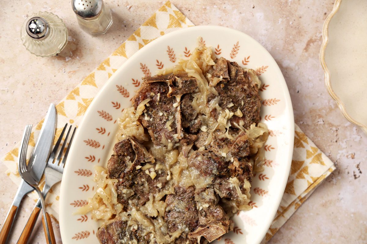 Close up of Taste of Home's Slow Cooker Lamb Chops served on a platter with a yellow linen on a beige marble surface.