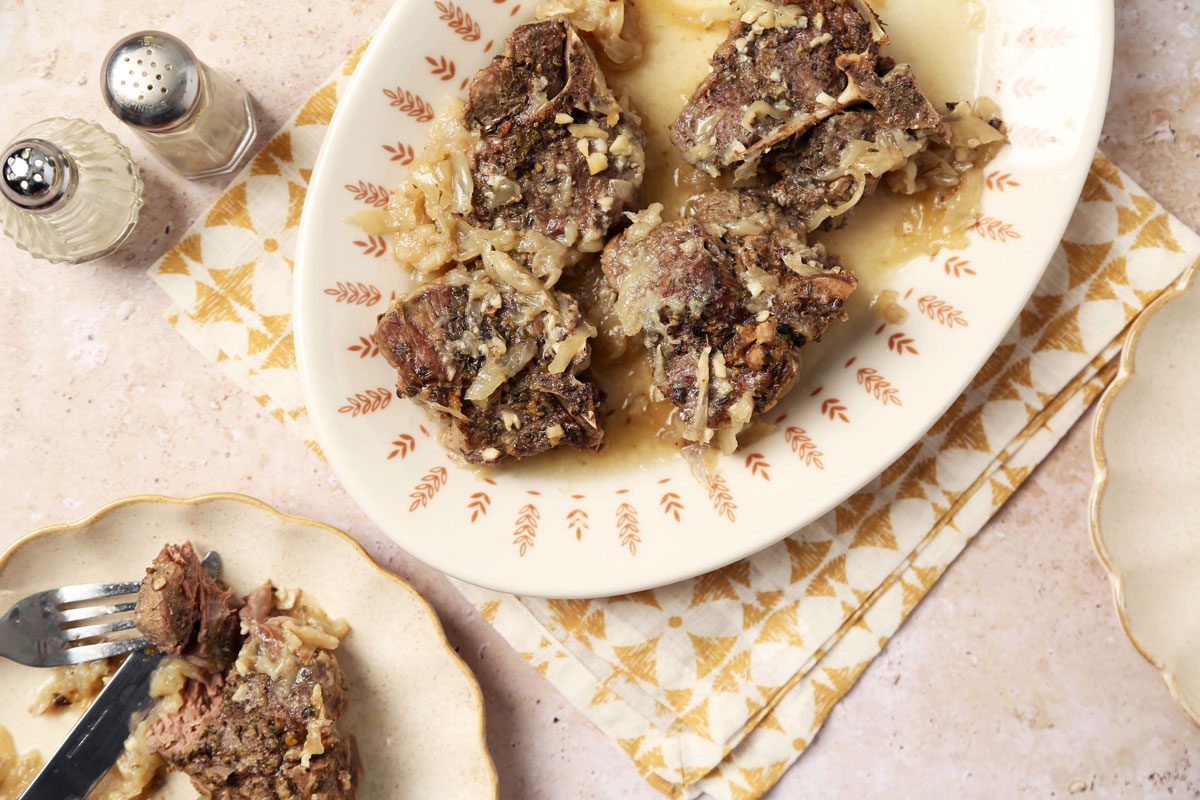 Close up of Taste of Home's Slow Cooker Lamb Chops served on a platter with a yellow linen on a beige marble surface.