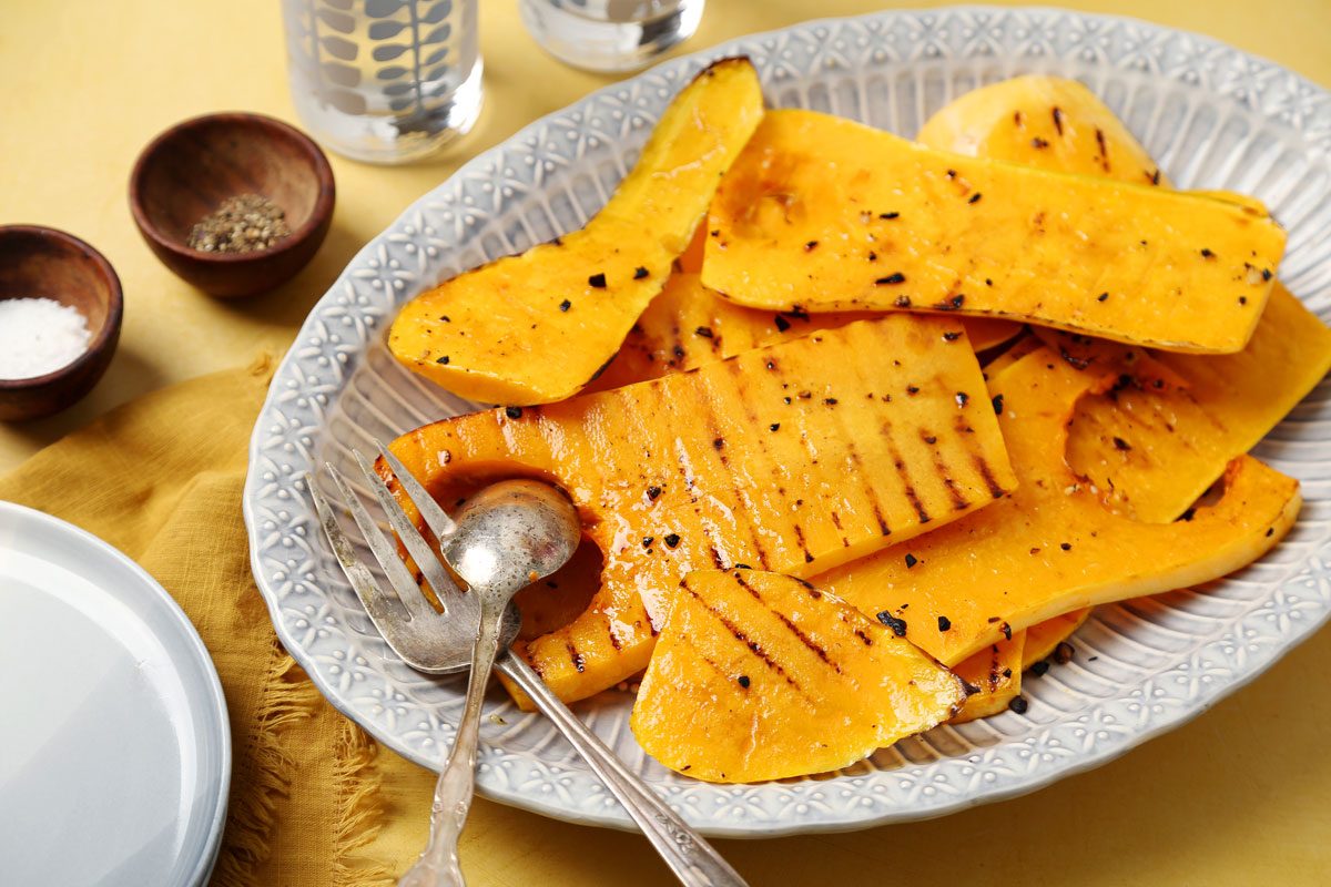 Close up of Taste of Home's Grilled Squash grilled butternut squash on a platter on a bright yellow surface.