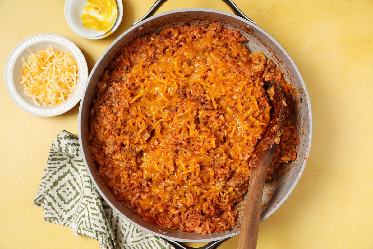 Process of making Taste of Home's Hamburger Casserole in a large nonstick skillet on a bright yellow surface.