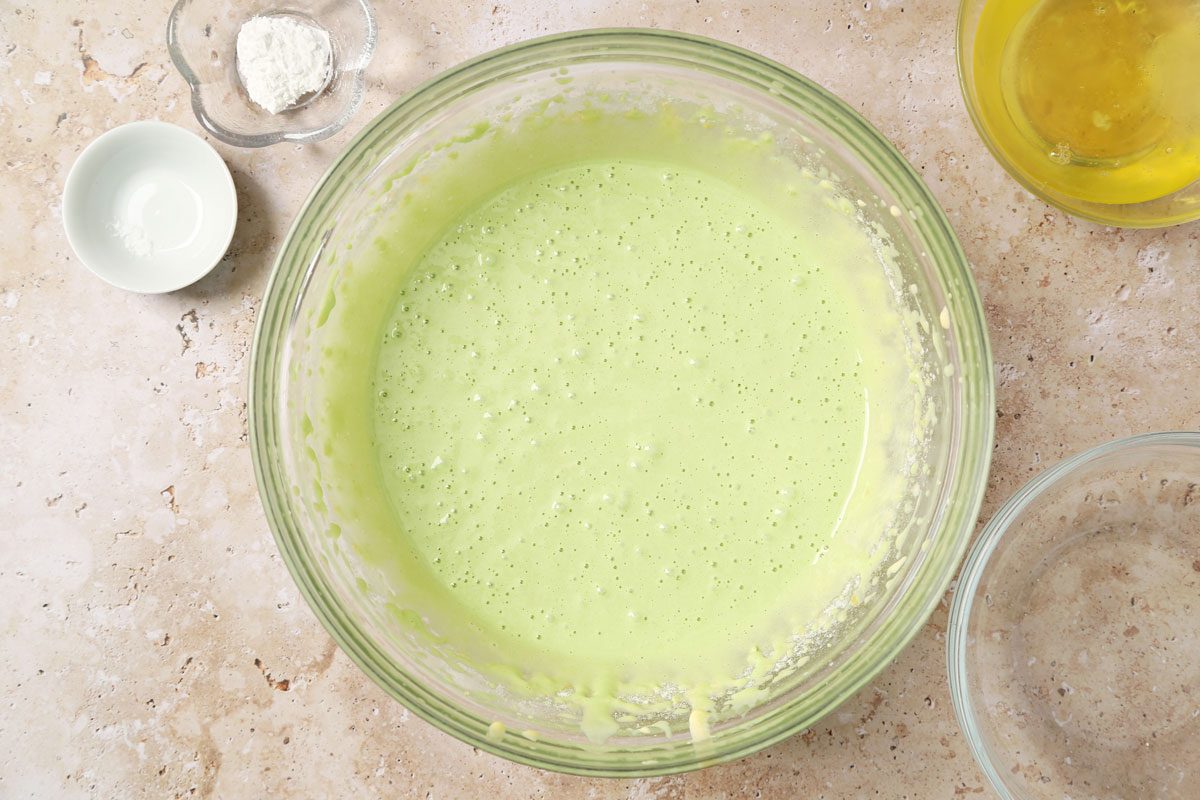 Process of making Taste of Home's Pandan Cake making the cake batter in a large mixing bowl on a brown marble surface.