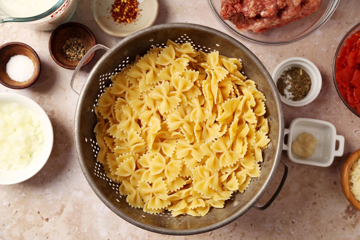 Process of making Taste of Home's Sausage and Bow Tie Pasta laid in a large red dutch oven on a brown marble surface.