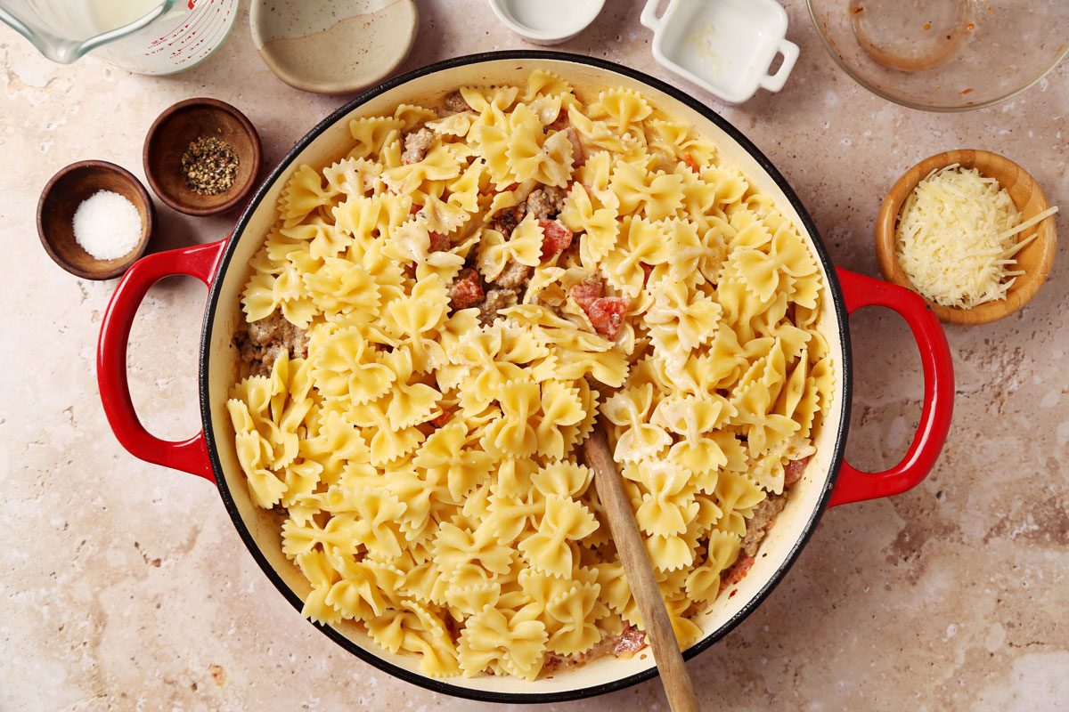 Process of making Taste of Home's Sausage and Bow Tie Pasta laid in a large red dutch oven on a brown marble surface.