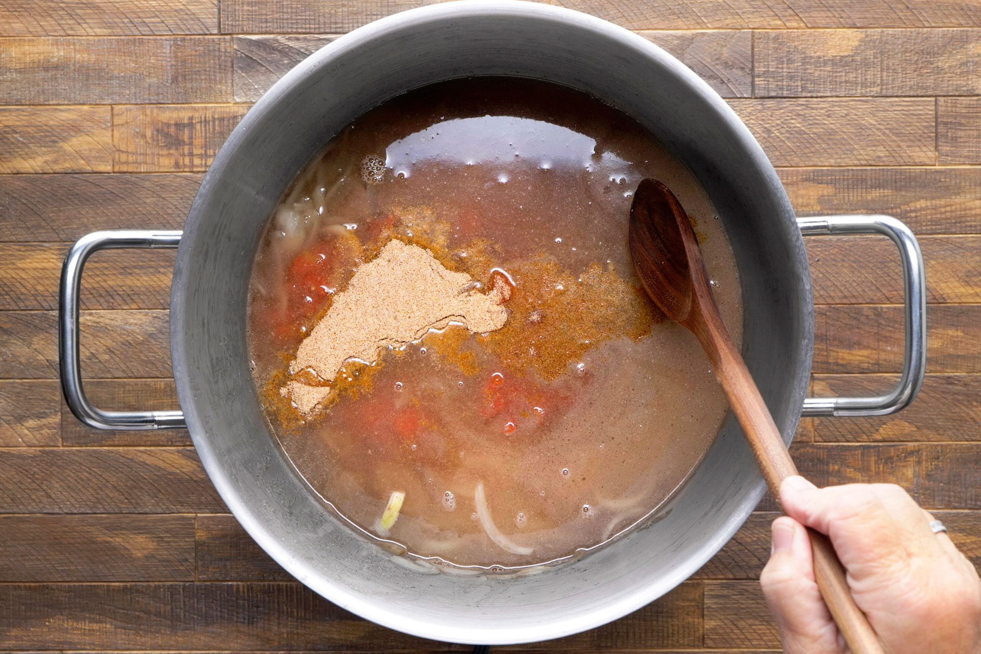 Pot is filled with a liquid, likely broth or stock, with chopped onions and diced tomatoes