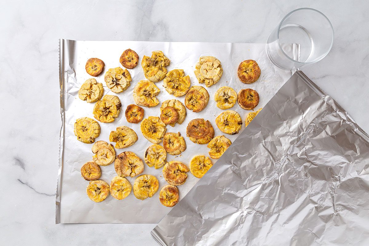 Smashed plantain slices on aluminum foil for step three of Air-Fryer Plantains recipe for Taste of Home