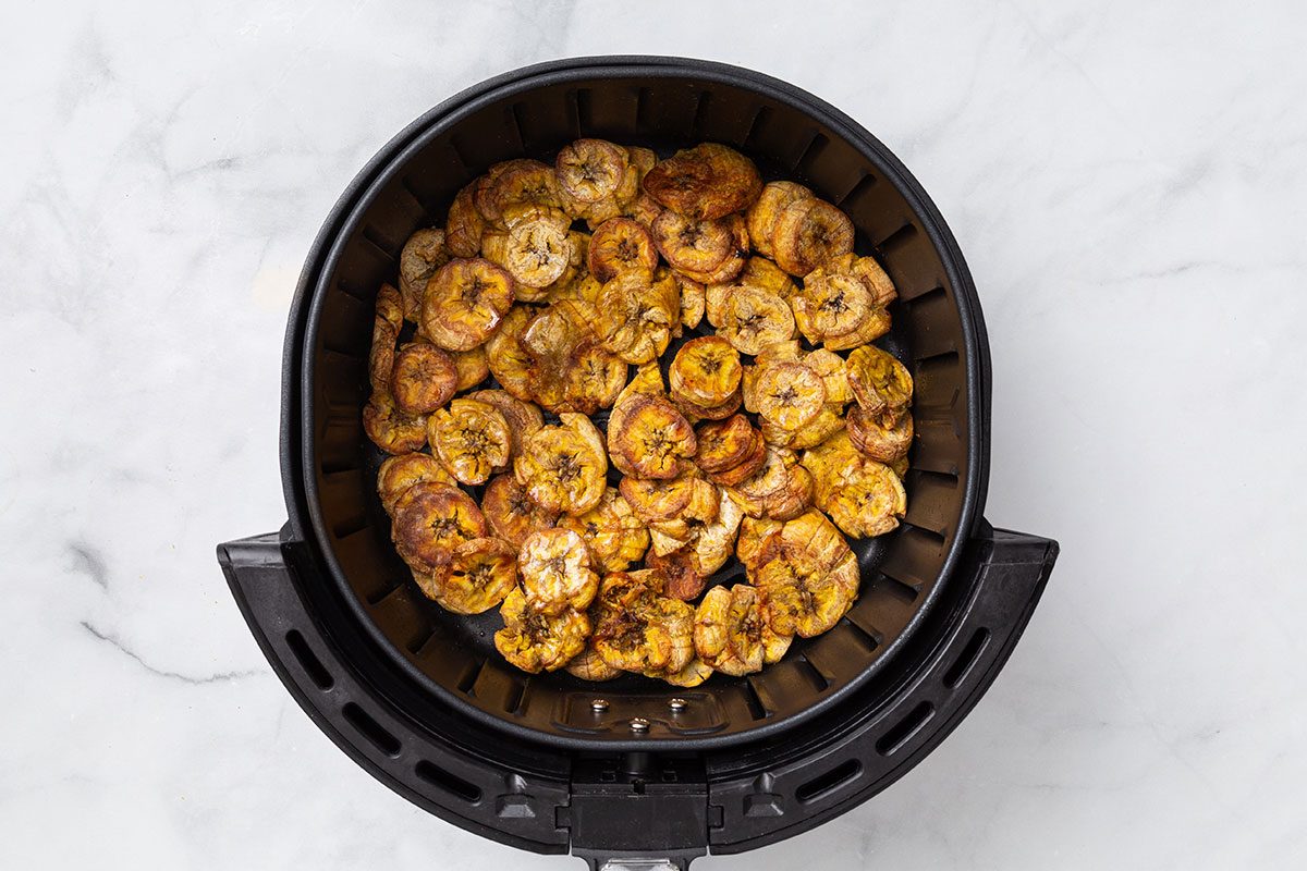 Cooked and flattened plantains in an air fryer basket for step four of Air-Fryer Plantain recipe for Taste of Home