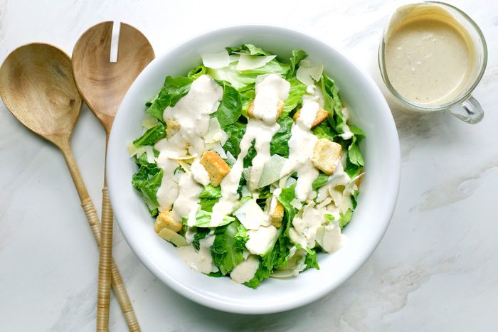 Caesar Dressing spread on a salad in a bowl with wooden spoons and dressing jar on side