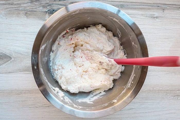 Combining the cream cheese with whipped topping and crushed candy.