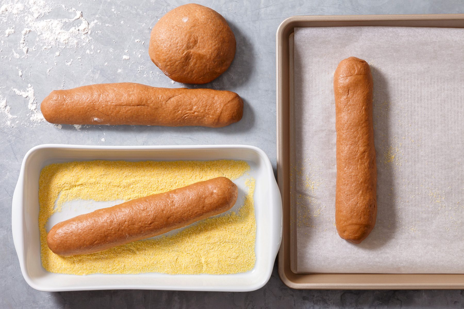 Overhead shot of place cornmeal in a shallow dish or tray; set aside; Turn dough onto a lightly floured surface and divide it into four equal-sized portions; Roll each into a smooth log about 8-inch long; press each loaf into cornmeal to lightly coat the bottom; Transfer loaves to a parchment-lined baking sheet about 4-inch apart; grey surface;