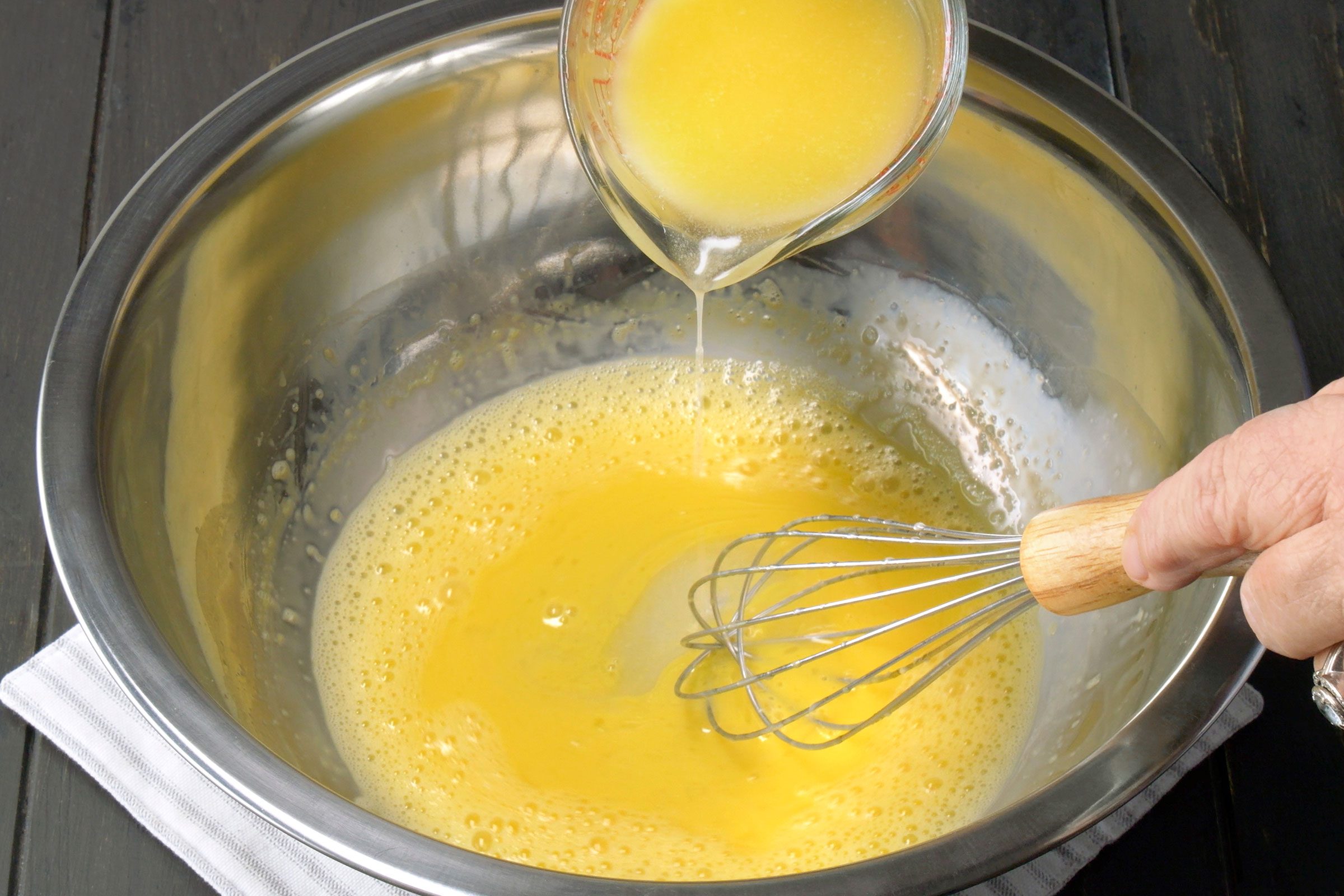 Adding warm melted butter in whisked egg yolks in a metal bowl