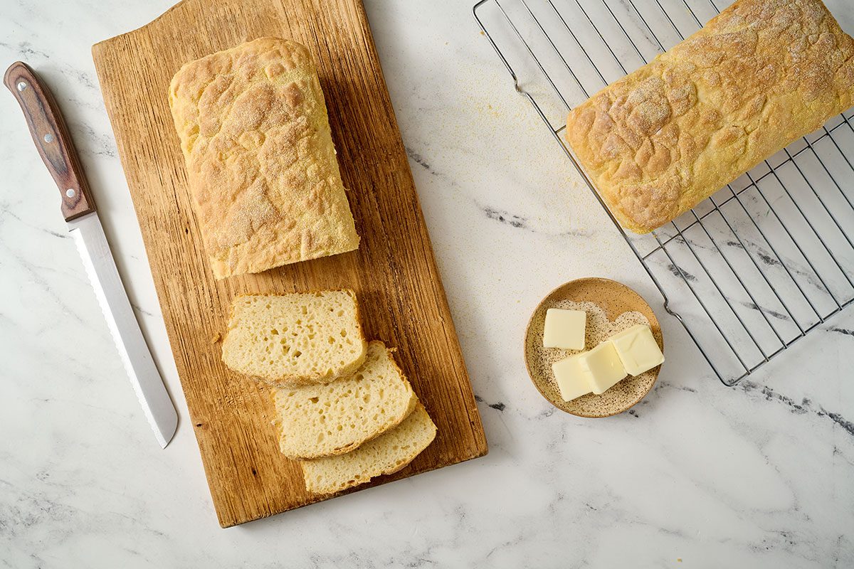 Overhead hero shot of the finished Taste of Home English Muffin Bread, sliced to showcase the airy texture and grainy cornmeal crust, served on a wooden cutting board.
