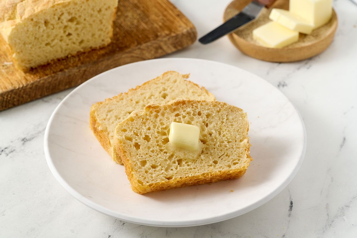 Close-up horizontal shot of the Taste of Home English Muffin Bread, highlighting the grainy cornmeal crust and the bread’s open crumb texture.