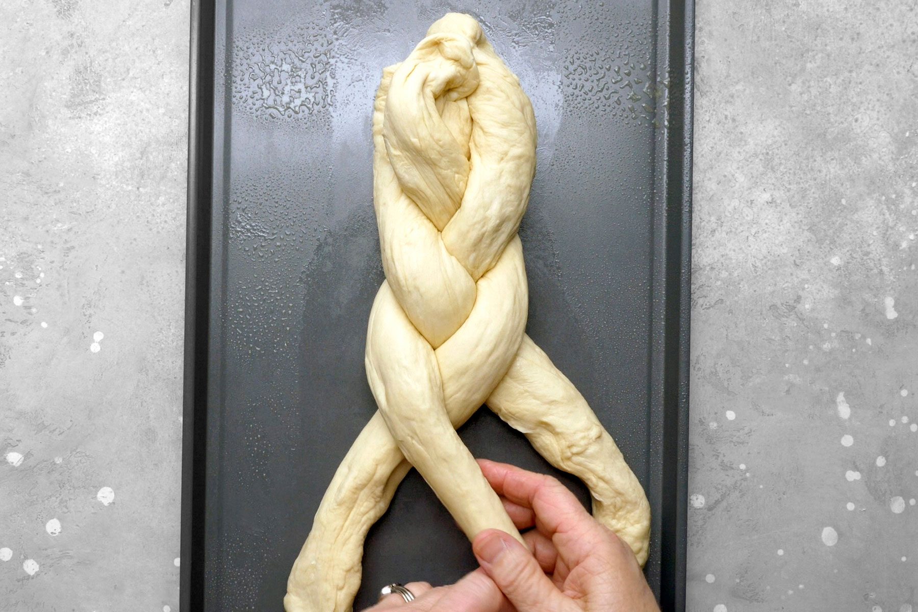 Ropes of dough on a baking sheet being braided together.