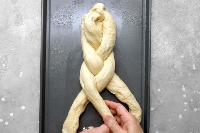 Ropes of dough on a baking sheet being braided together.